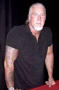 White male with gray hair and arm tattoos wearing a black shirt