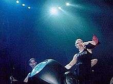 Madonna sliding down from a car on stage, flanked by two female dancers