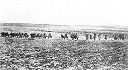 A line of men on horses charge across an open field towards the camera.