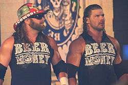 Two adult white males wearing black shirts with "Beer Money" in green text on the front. Both have long black hair, one wearing a cowboy hat.