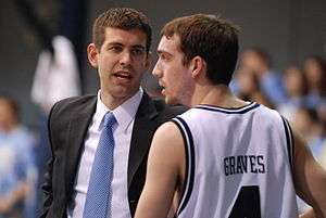 Stevens looks at a player as he talks with him. The players eyes are turned toward the basketball game to Stevens' left.