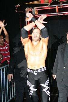 Adult white male wearing black and white wrestling gear doing hand symbols.