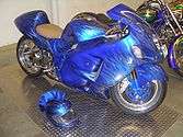 An motorcycle with fully enclosed bodywork painted in iridescent blue with flames, and a helmet painted in the same color scheme, with a matching blue fur crest on the helmet.