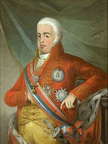 Three-quarter length portrait of a man with white hair, facing left, wearing a red coat and yellow breeches and waistcoat, a prominent sash with sword and various medals and ribbons. His right hand is tucked into the waistcoat, his left elbow rests on a pillar.