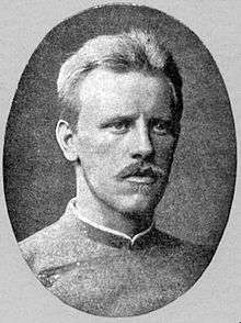 Head and shoulders of a young, fair-haired man with a blond moustache, looking to the right. He is wearing a jacket buttoned to the neck.