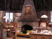 Interior photograph of the Leconte Memorial Lodge. Stone walls and several laden interpretive display tables surround a large stone fireplace with a bas-relief of Joseph LeConte.