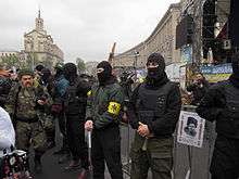 A line of five Patriot of Ukraine members (some with bats) providing security at a meeting organized by Right Sector activists, at the Euromaidan's main stage